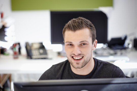 Young man working in office, looking at camera