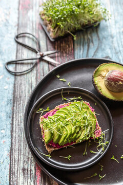 Slice of bread with beetroot hummus, slices of avocado and cress