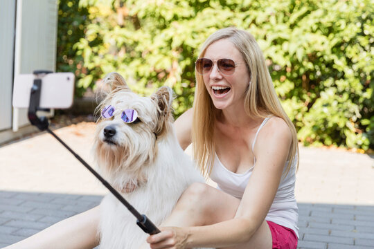 Happy woman taking a selfie with her dog wearing sunglasses