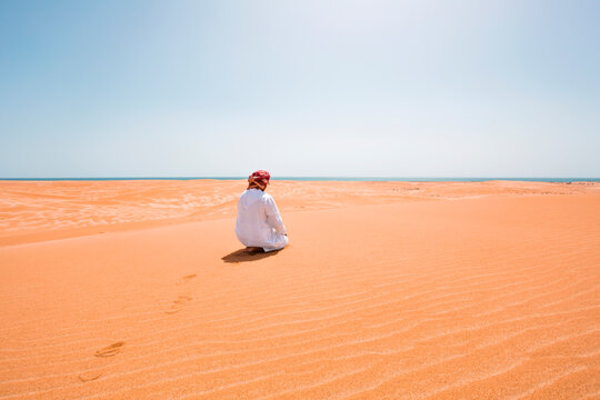 Bedouin in National dress praying in the desert, rear view, Wahiba Sands, Oman