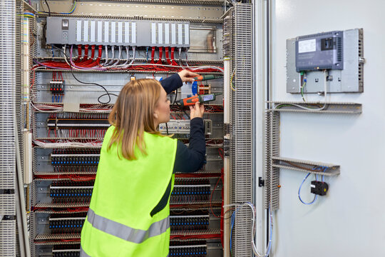 Female electrician working with voltmeter at fuse box