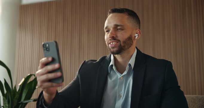 Businessman, hotel and video call with phone, wave and smile for travel, contact and chat. Male person, happy and greeting with hello, accommodation and conversation for virtual meeting on work trip