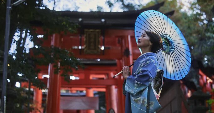 Cinematic low shot of beautiful Japanese woman in kimono holding umbrella near torii gates