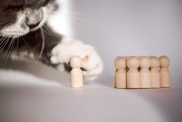 Cat paw reaching for a wooden figurine in front of a group of six wooden figures on a light...