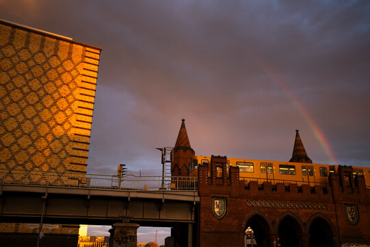 Rainbow cuts through sunset sky and clouds over a Berlin bridge where urban architecture forms a landmark skyline scene in Germany during dusk light