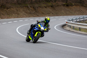 Motorcyclist in grey and neon yellow gear leaning into a sharp corner on a blue sport bike on a winding mountain road.