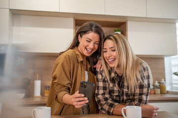 Happy young women friends laughing watching smartphone together