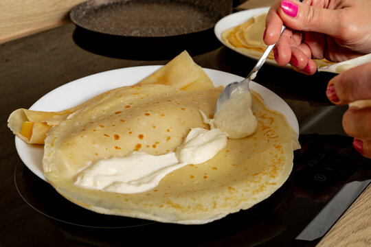 Fried golden yellow pancake batter on a white plate, rolling pancakes, spreading white cream cheese on pancakes,