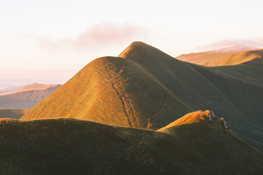 View of rolling green hills bathed in the soft, warm glow of the setting sun, creating a serene and inviting landscape, Mont-Dore, Auvergne-Rhone-Alpes, France.