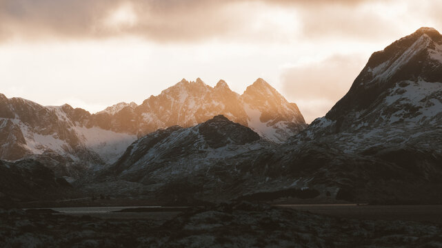 View of snow-dusted peaks pierce the heavens in a majestic display of nature's grandeur, bathed in the warm glow of the setting sun, Fredvang, Nordland, Norway.