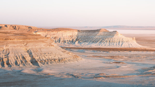 View of layered cliffs cascading towards an endless horizon, where the sun kisses the earth with hues of gold and dust, Aktau, Mangystau Region, Kazakhstan.