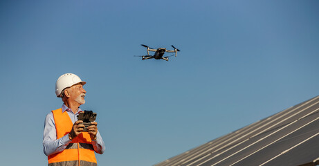 Senior male environmentalist operating a drone near solar panels at a renewable energy site under clear blue sky