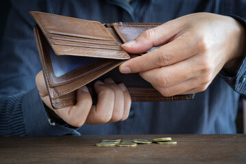 Poor man hands opening empty leather wallet with few coins on wooden table. Financial crisis, debt, and poverty and expenses are insufficient.concept.