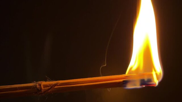 A bundle of wax-coated wooden splinters ignites into a bright, steady flame against a dark background. The burning wood and melting wax crackle and hiss merrily as they combust.