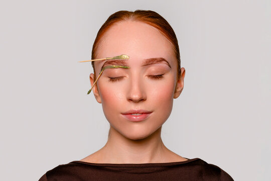 Woman poses with closed eyes and green object on her brow in a simple setting