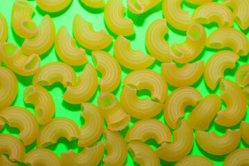 Dry elbow pasta shapes are densely scattered across a bright lime green background, creating a dynamic culinary pattern. This contrasting food photo is excellent for illustrating pasta recipes, menu d