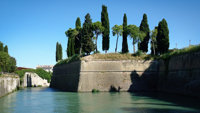 Alte Stadtmauern mit Zypressen bepflanzt und umgeben von einem Wasserkanal in der N&auml;he des Gardasees in Peschiera del Garda, Italien