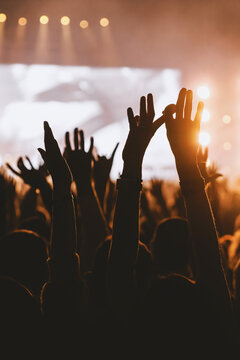 Silhouetted crowd raising hands and rock signs at concert