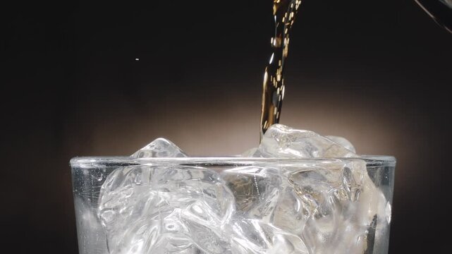 Close-up shot of glass top and cola drink being poured into a glass. Visible fizzy splash and rising carbonate bubble close up on dark background.