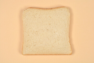 A single square slice of fresh white sandwich bread is centered on a plain light beige background shot from a top down perspective.