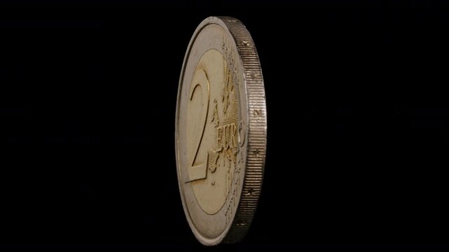 Two  euro coins spin  around their  axis  on black background.