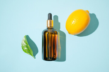 Vitamin C facial serum or essential oil, fresh lemons, green leaves on blue background flat lay top...