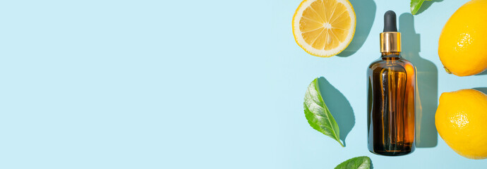 Vitamin C facial serum or essential oil, fresh lemons, green leaves on blue background flat lay top...
