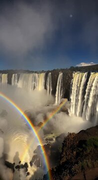 Breathtaking night view of Iguazu Falls with a rare double moonbow appearing in the mist under a starry sky
