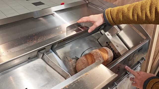 16 february 2026, Aachen, Germany. Lidl discounter store. Caucasian man putting a bread in a bread cutting machine, select and push a button. The machine starts cutting bread, in slices. Cheap superma