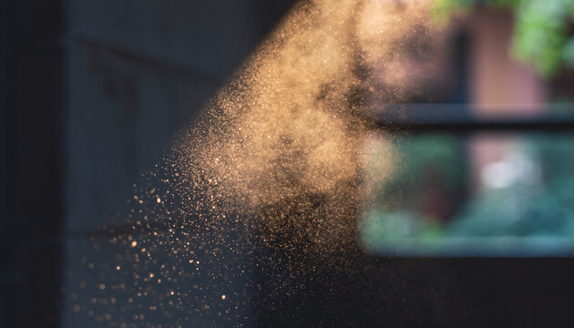 Dust particles dispersing in the air against a blurred background.