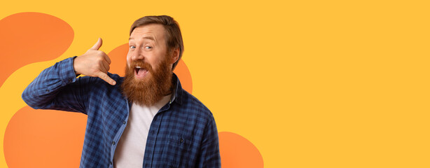 A man showing a phone gesture with his hand while smiling widely. He has a beard and wears a...
