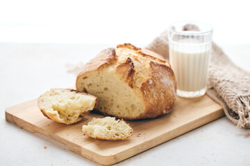 Sliced artisan sourdough bread with airy crumb on wooden board, glass of milk, and knitted cloth. Ideal for culinary, baking, and food photography projects.