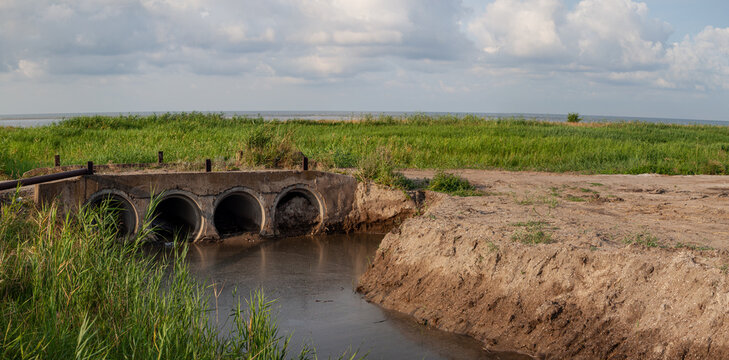 Old drainage culvert structure spanning shallow water channel in rural wetland near horizon sea, South Ukraine