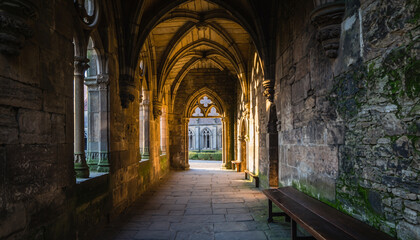 Ancient stone corridor with arches and sunlight streaming through.