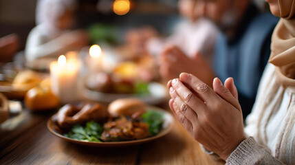 Fototapeta premium Family praying or having dinner at table faceless, Ramadan celebration or iftar at home, food and religious holiday, breaking fast together, defocused background, with copy space