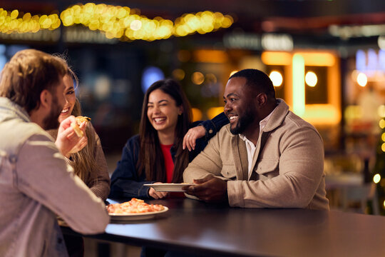 Friends Laughing and Sharing Pizza at Night Market Bar During Casual Social Gathering