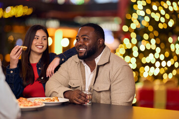 Fototapeta premium African-American Man and Friend Sharing Pizza at Night With Holiday Lights Behind Them