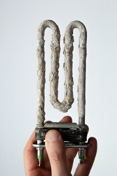 Hand holding used washing machine tubular electric heater covered in limescale.