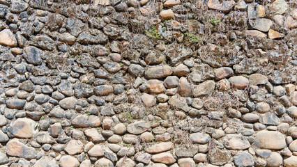 Fototapeta premium Weathered stone wall background with irregular rocks and dry grass