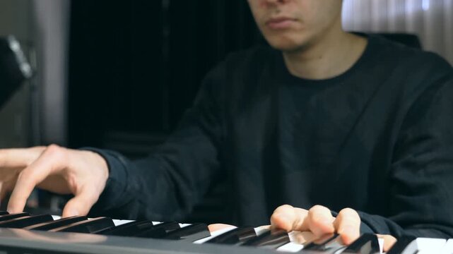 Male musician playing at synthesizer at sound recording studio. Young man plays solo of music. Close up fingers of pianist at the piano keys. Slow motion