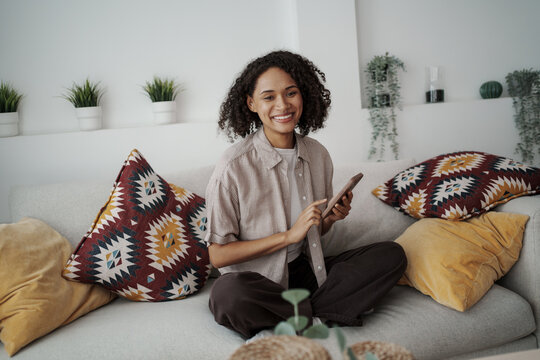 Relaxed Woman Teaching With Smartphone In Cozy Setting Surrounded By Greenery And Soft Cushions