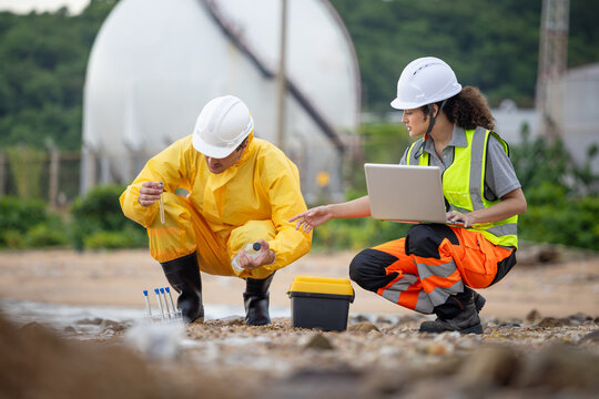 Team of specialized technicians performing water quality testing and ecological monitoring at coastal site with gas storage tanks, Environmental researchers analyzing water samples and recording data