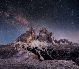 Obraz premium Nighttime alpine landscape with rugged mountain peaks silhouetted against a vivid Milky Way and starry sky, evoking solitude, adventure, and cosmic wonder in a remote high‑altitude setting.
