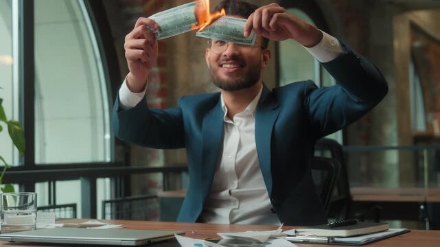 Hindu rich business man burning money financial crisis at workplace overspending finance Arabian male office guy businessman happy play smiling burn cash joke waste holding paper banknotes with fire