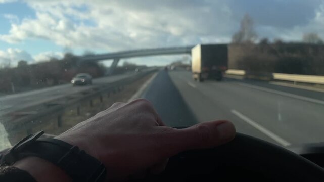 Closeup of commercial driver steering wheel, Focused male commercial driver maneuvering fast lane changes, Closeup of male professional driver handling steering wheel at high speed under cloudy sky 