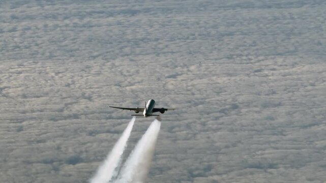 aerial top video view of an wide-body passenger airplane with contrails produced by each engine, flying in front below on same track in the same direction - 4k aerial video footage