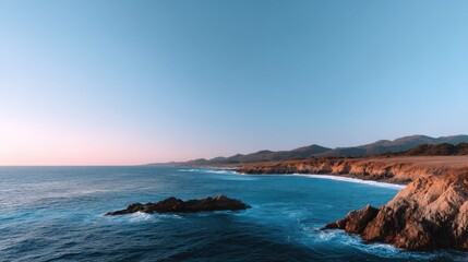 Serene Coastal Landscape at Dusk with Gentle Waves and Misty Mountains in the Background Reflecting a Tranquil Ocean Horizon Under a Clear Blue Sky