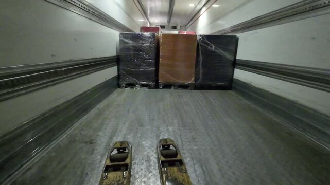 First person point of view shot of an electric pallet jack driving into a semi trailer to collect a shrink wrapped pallet