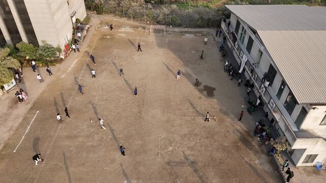 Drone footage over a schoolyard with students playing and gathered, aerial view.