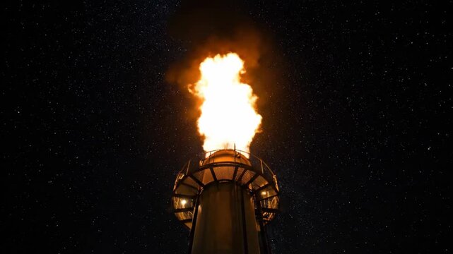 Industrial flare stack burning gas at night under a starry sky. Large flame from a refinery chimney against the Milky Way. Energy production and heavy industry concept